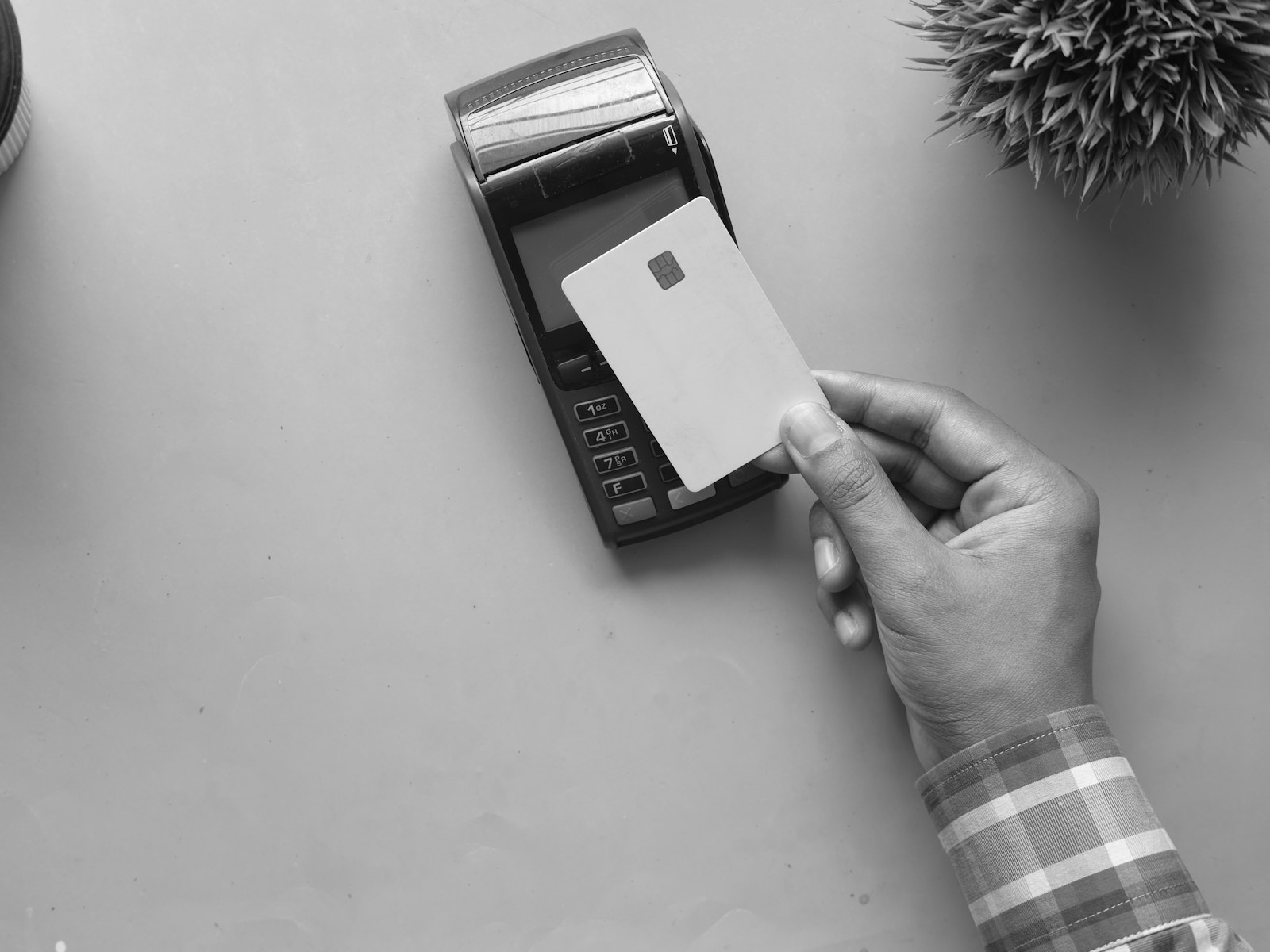A hand holding a blank card next to a payment terminal, in black and white